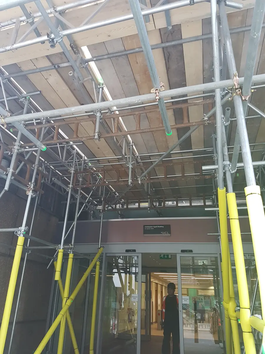 A scaffold built over a building entrance, with yellow guards on the uprights