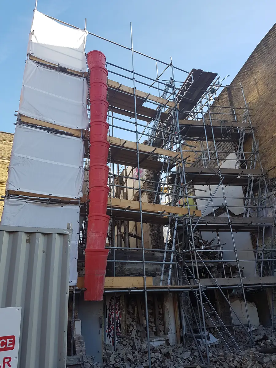 A red rubbish chute running down a scaffold